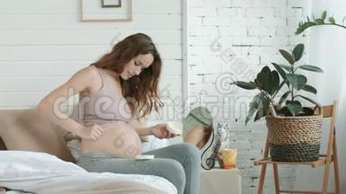 年轻孕妇在卧室的孕妇腹部涂护肤霜。